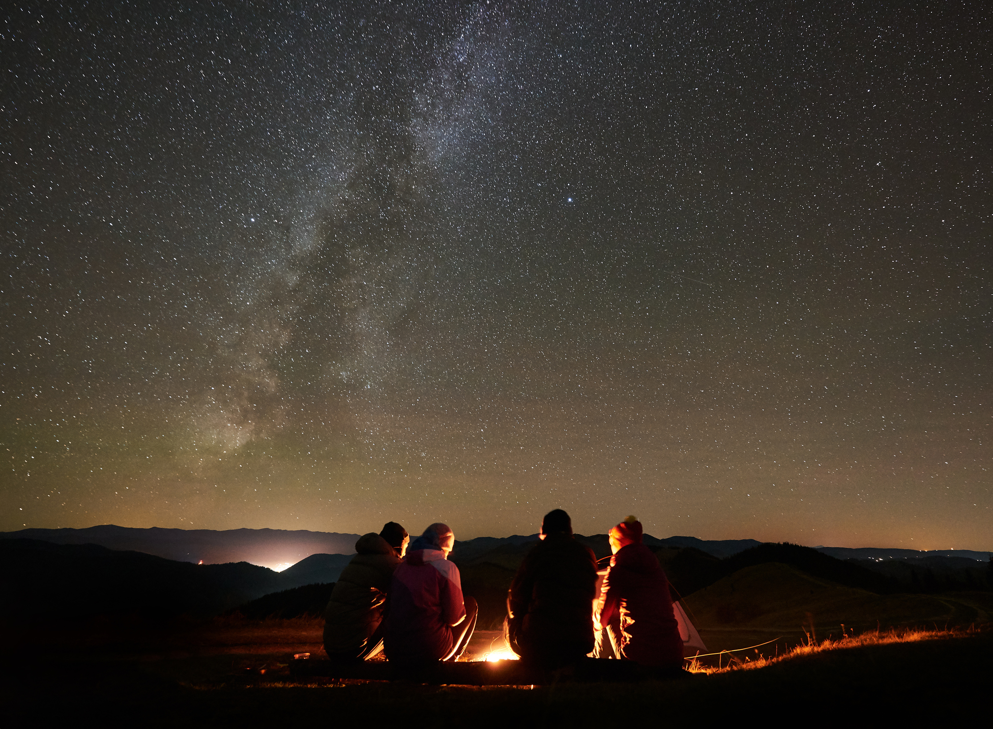 Friends resting beside camp, campfire under night starry sky