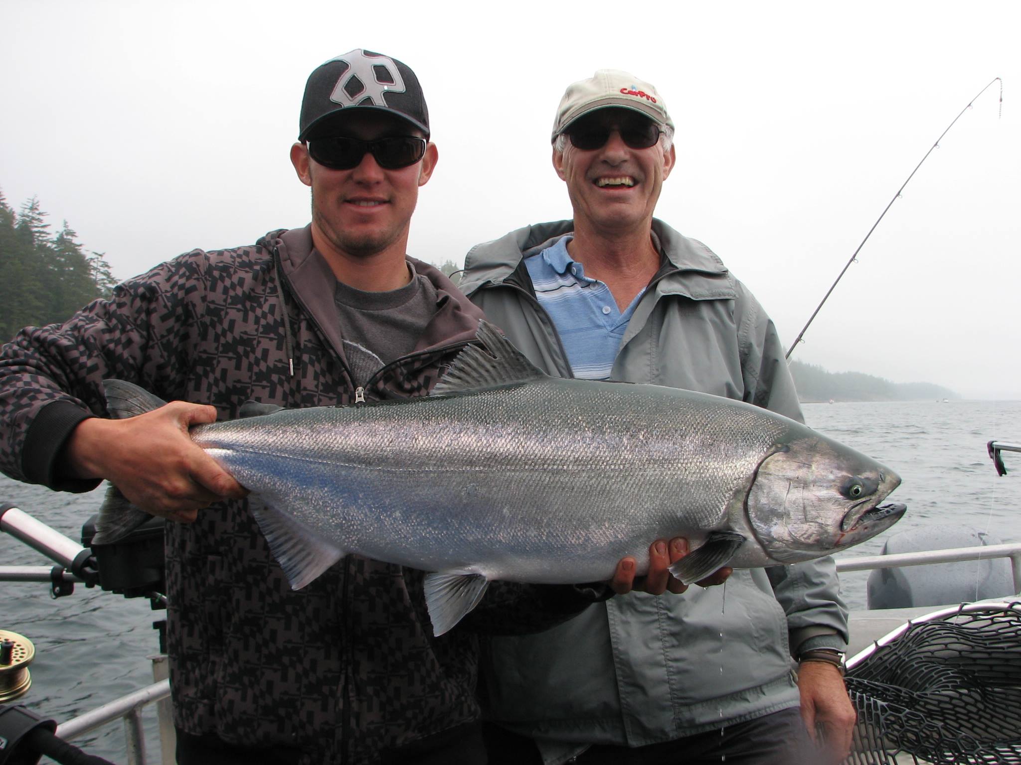 Two men holding a large fish while standing in a boat on the ocean.