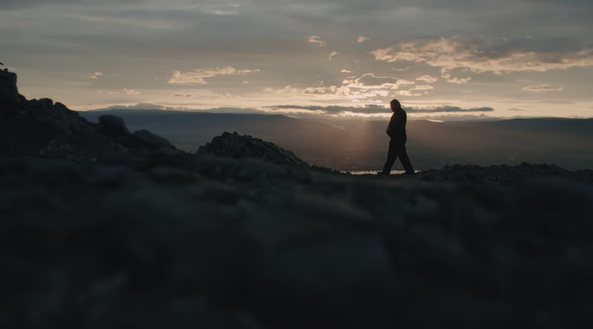 man walking along the mountain with sky in background