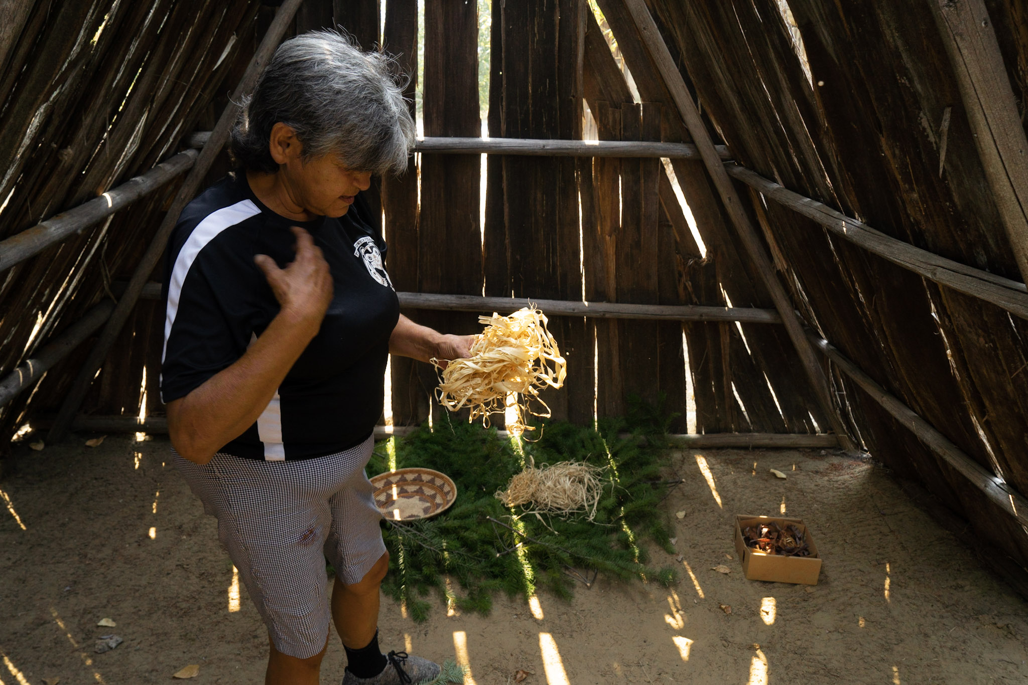 A woman inside a hut with some wood shavings for a fire