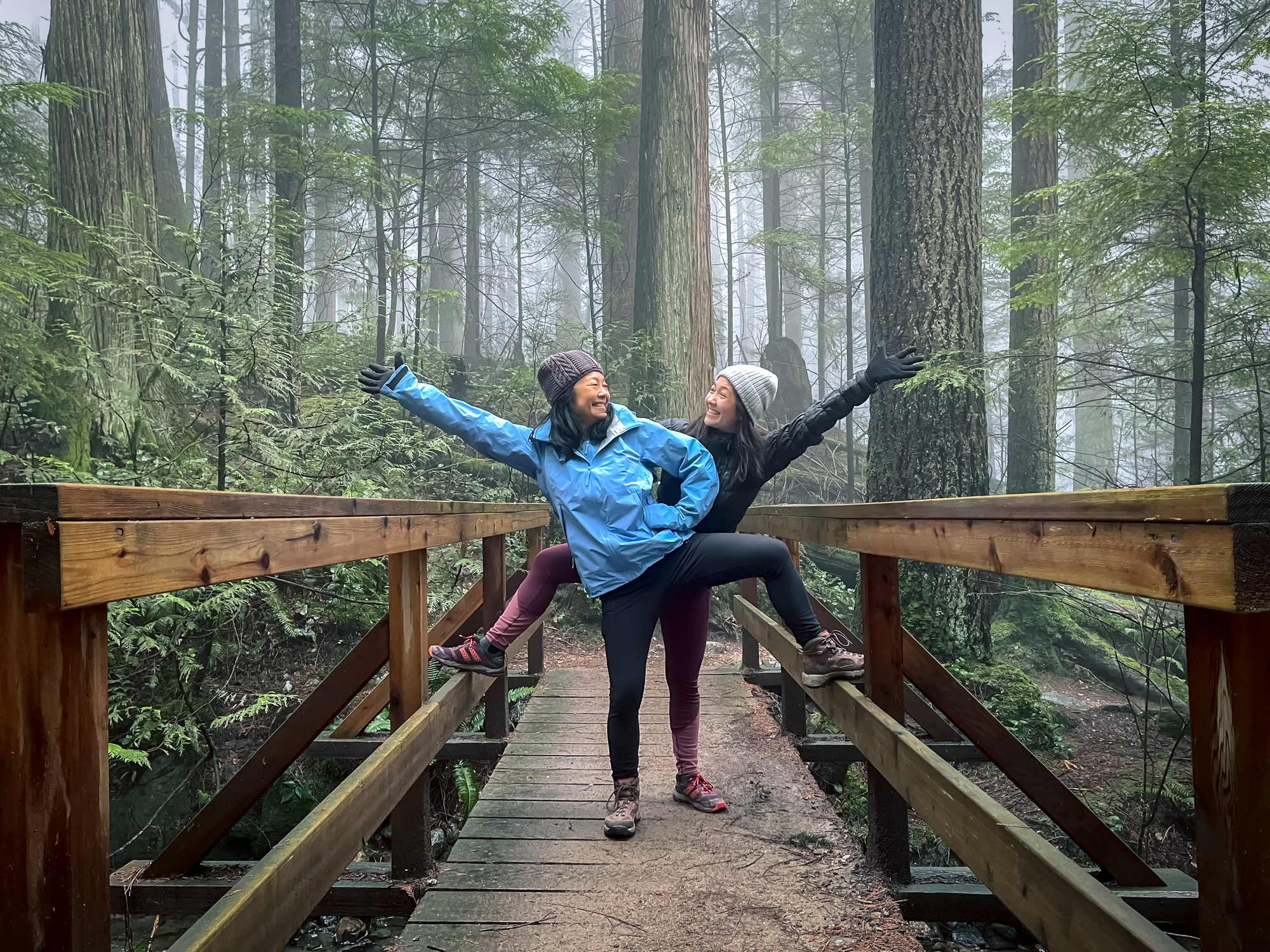 two women standing on a bridge in the woods.