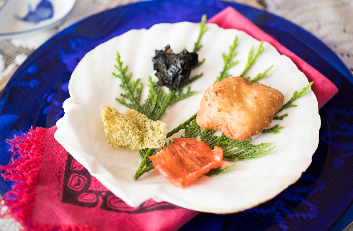 Salmon and other indigenous food on a scallop shaped plate.