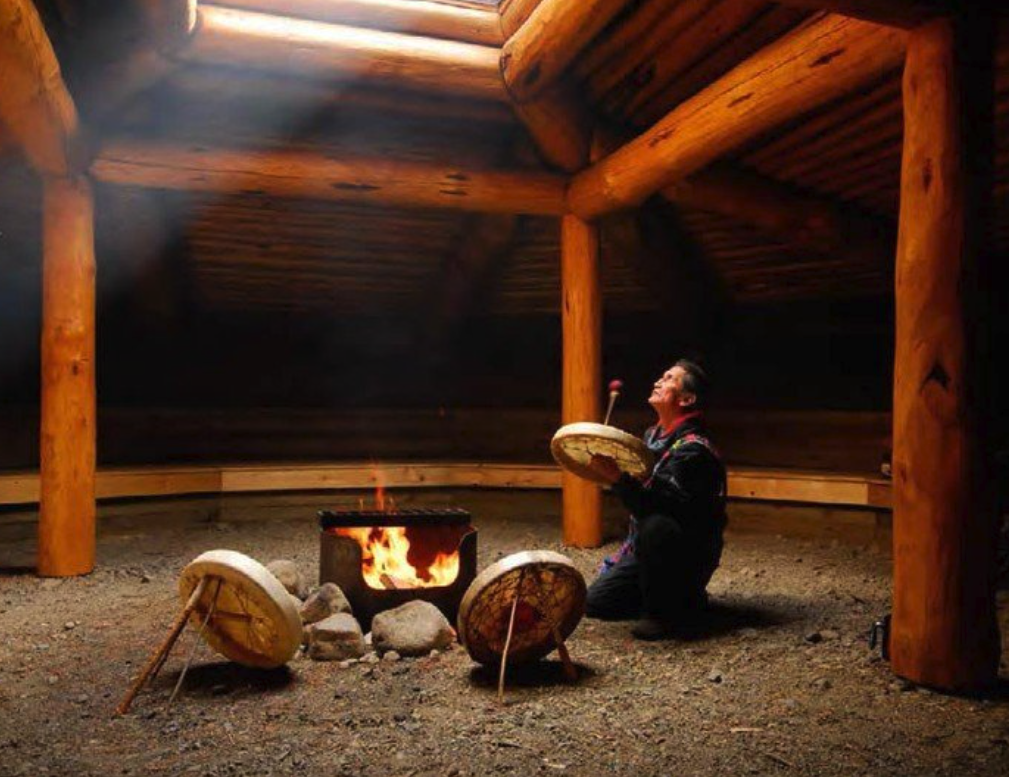 Indigenous person playing drums next to fire