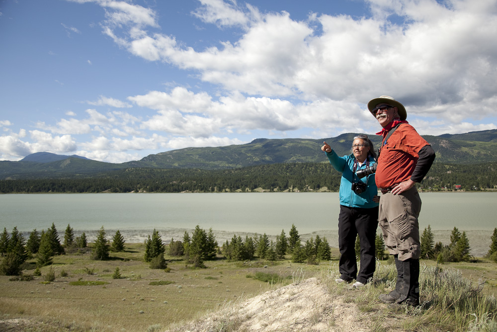 A man and woman stand at the top of a sandy hillside next to a body of water