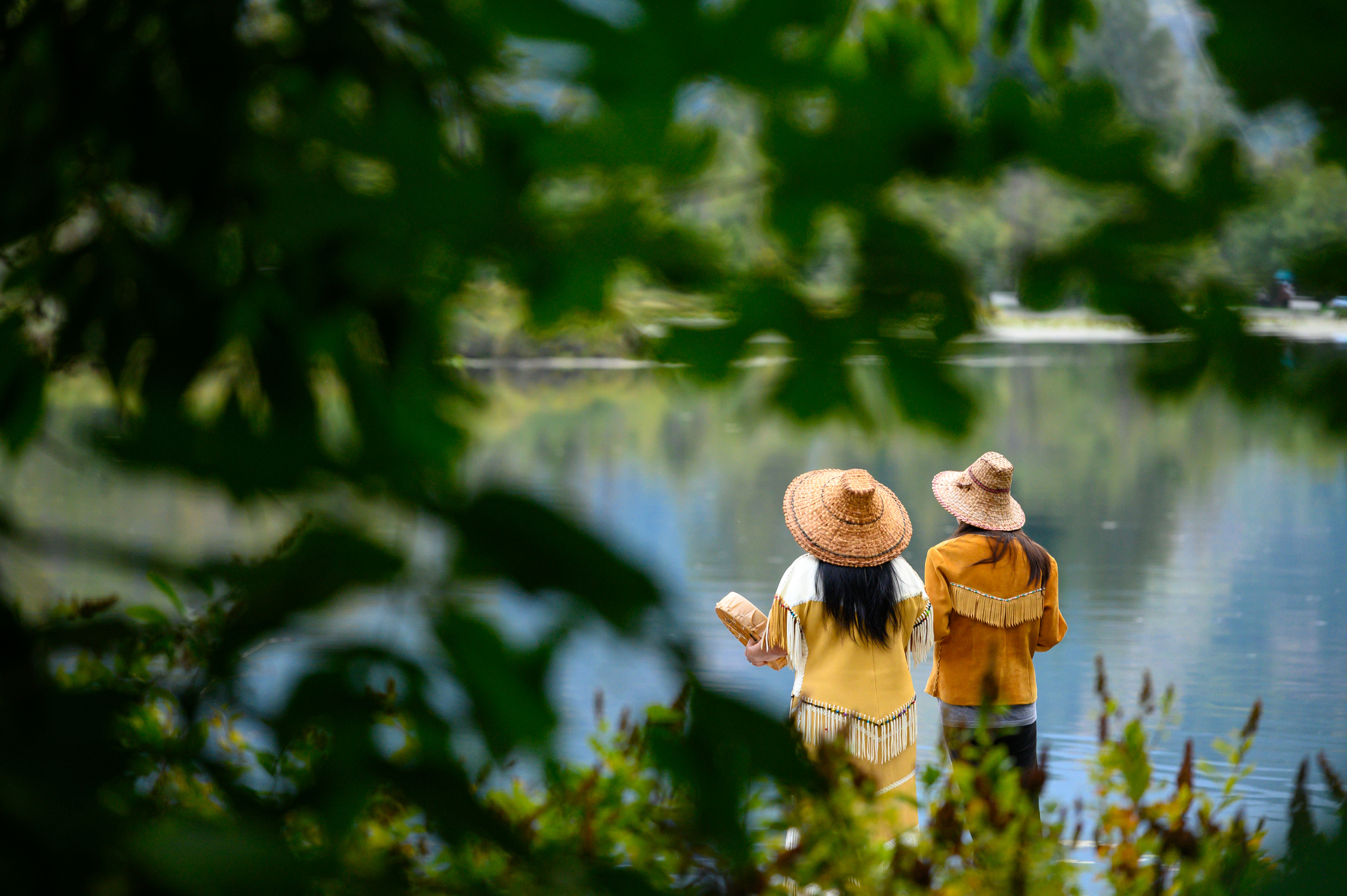 Two people standing on a dock with a drum looking at the water