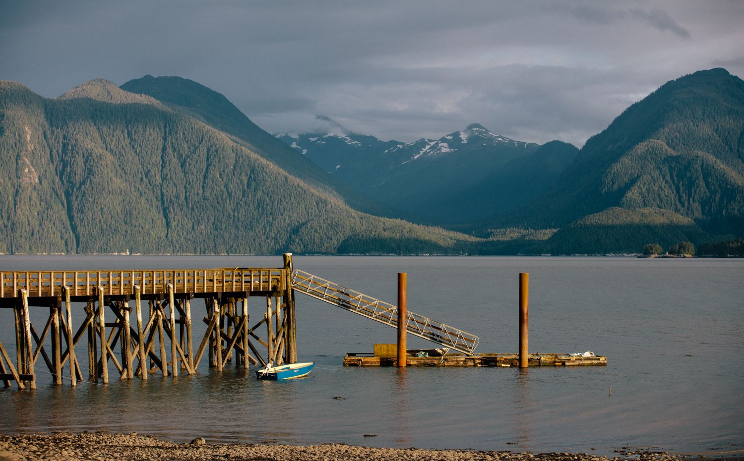 A dock in the water with a small boat and the mountain range in the background