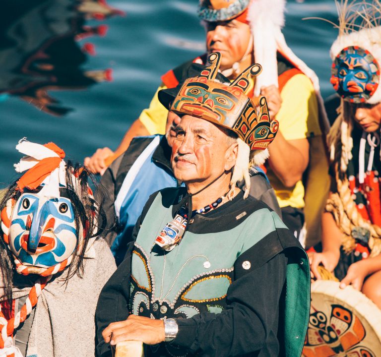 A man wearing traditional clothing in a canoe with a drum