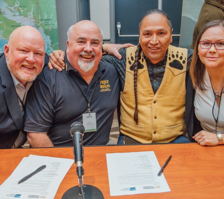 Four people sitting at a desk with a microphone smiling for a photo.