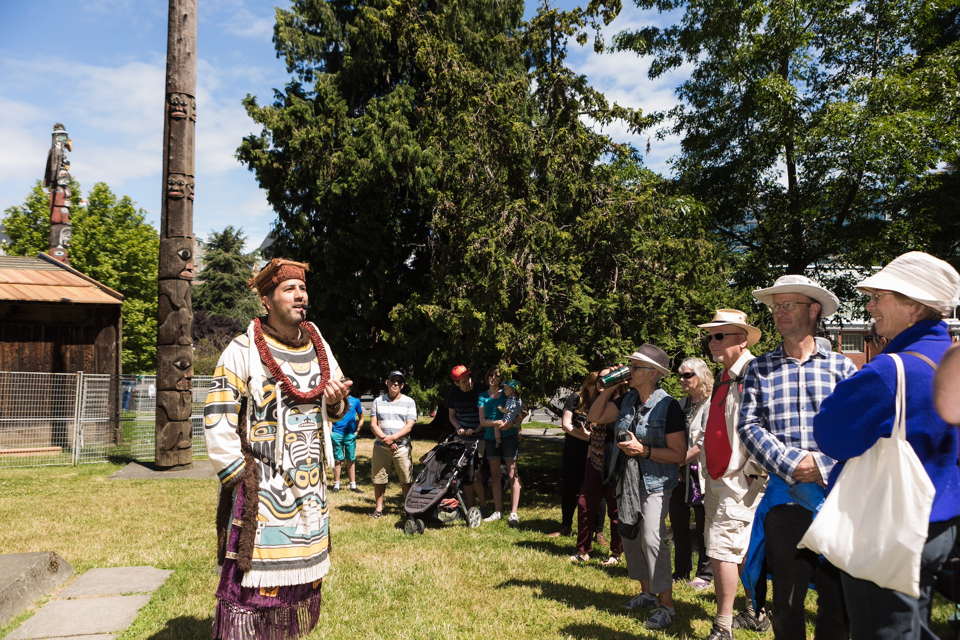 A man wearing traditional Indigenous clothing speaks to a crowd