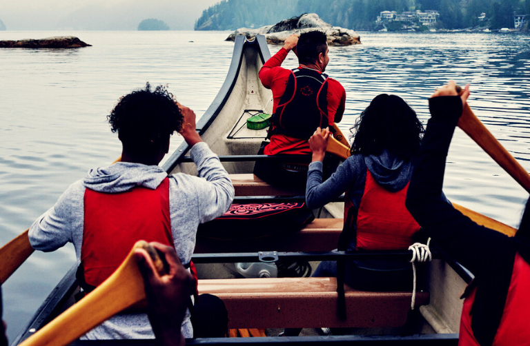 Four people in a canoe on a lake between the mountains