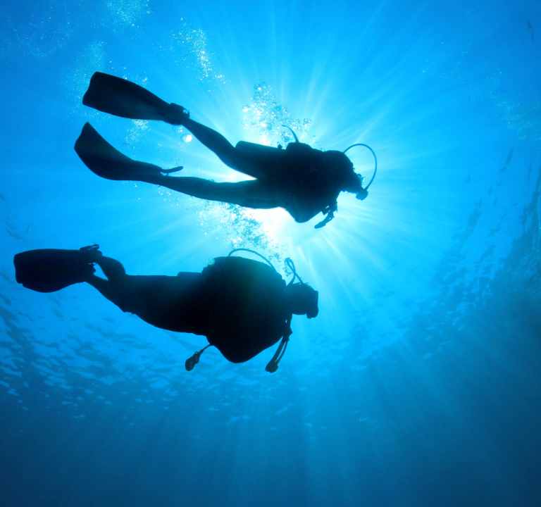 Two divers underwater with sun rays shining through the surface.