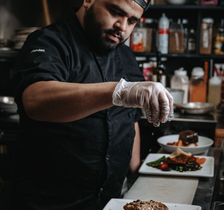 Chef garnishing food on plates in a professional kitchen.