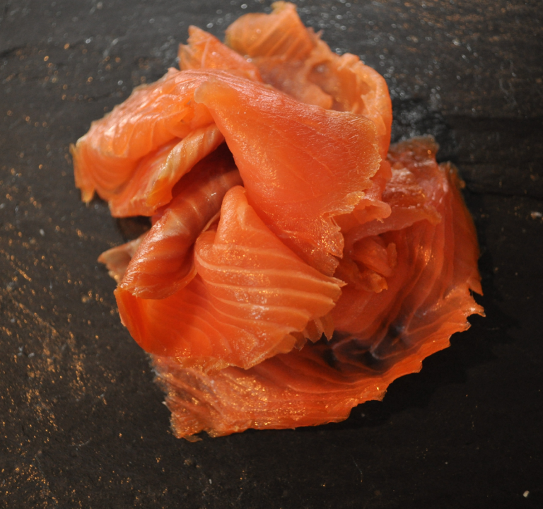 Slices of smoked salmon arranged on a dark surface.