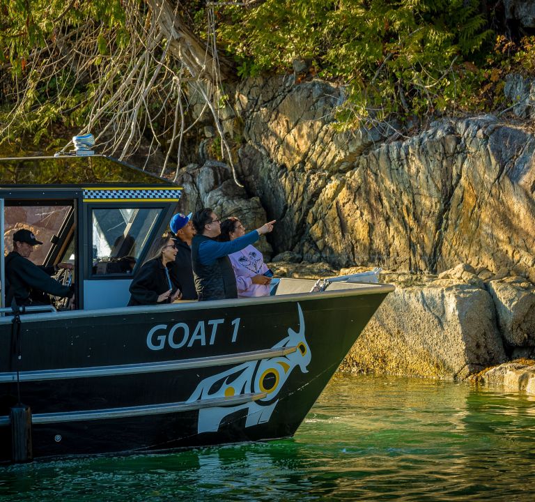 Three people on a boat named GOAT 1 pointing towards rocky shore.